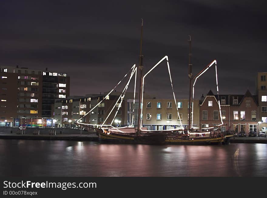 Nightscape of a river harbour in Holland with a decorated sailship in the foreground. Nightscape of a river harbour in Holland with a decorated sailship in the foreground