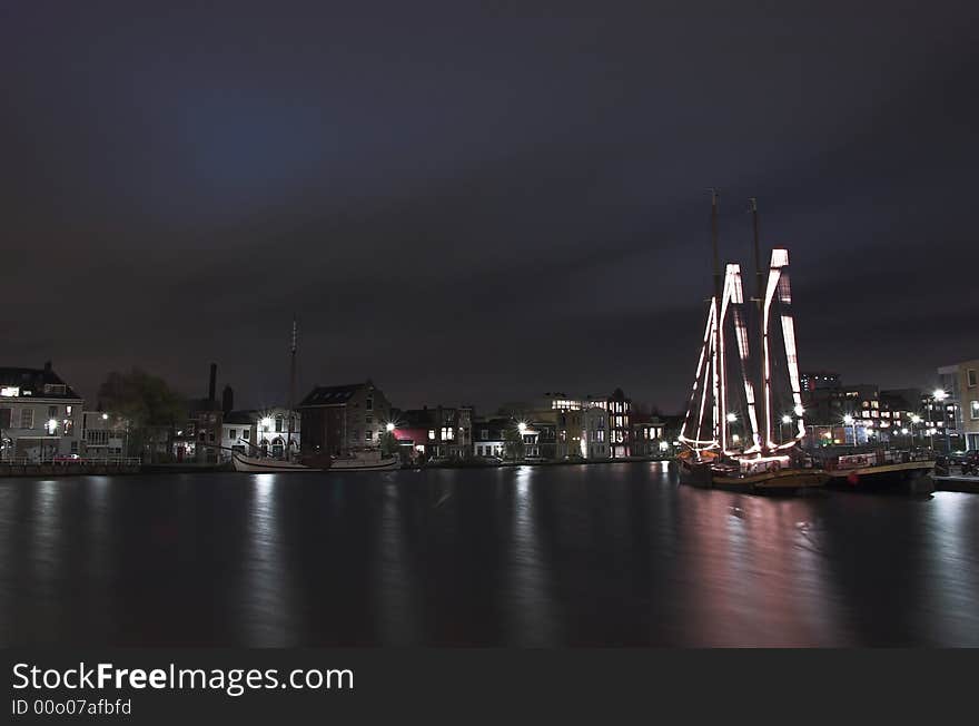 Nightscape of a river harbour in Holland with a decorated sailship in the foreground. Nightscape of a river harbour in Holland with a decorated sailship in the foreground