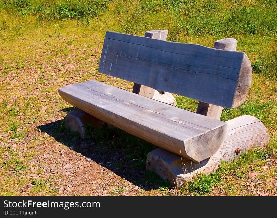 Empty grey log bench in a grassy clearing on a hot summer day.