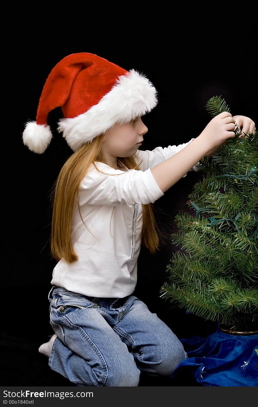 Small girl in jeans and Santa hat decorates her Christmas tree. Small girl in jeans and Santa hat decorates her Christmas tree.