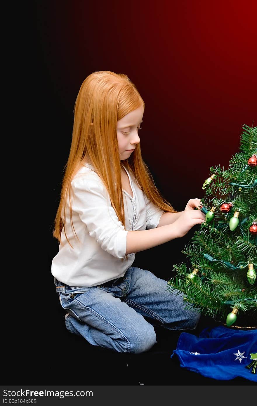 A small red haired girl decorates a miniature tree - black to red gradient background. A small red haired girl decorates a miniature tree - black to red gradient background.