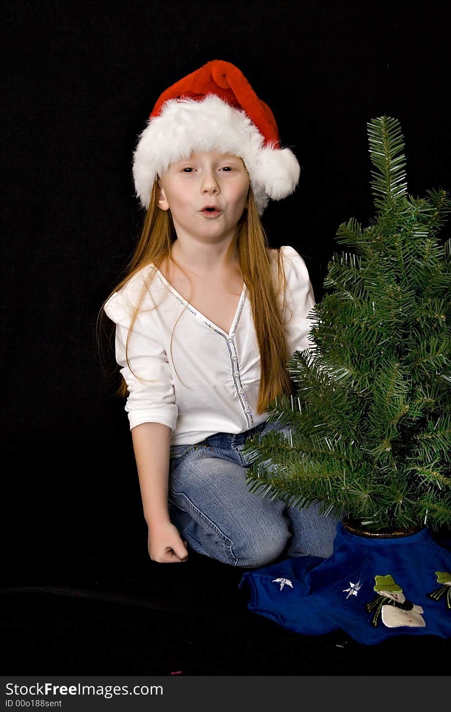 A small red head girl in Santa hat decorates her Christmas tree - mouthing the words Ho-Ho-Ho. A small red head girl in Santa hat decorates her Christmas tree - mouthing the words Ho-Ho-Ho.