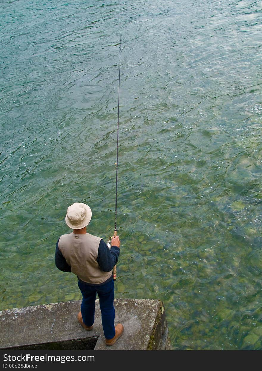 Fly fisher with a rod standing at the riverside. Fly fisher with a rod standing at the riverside