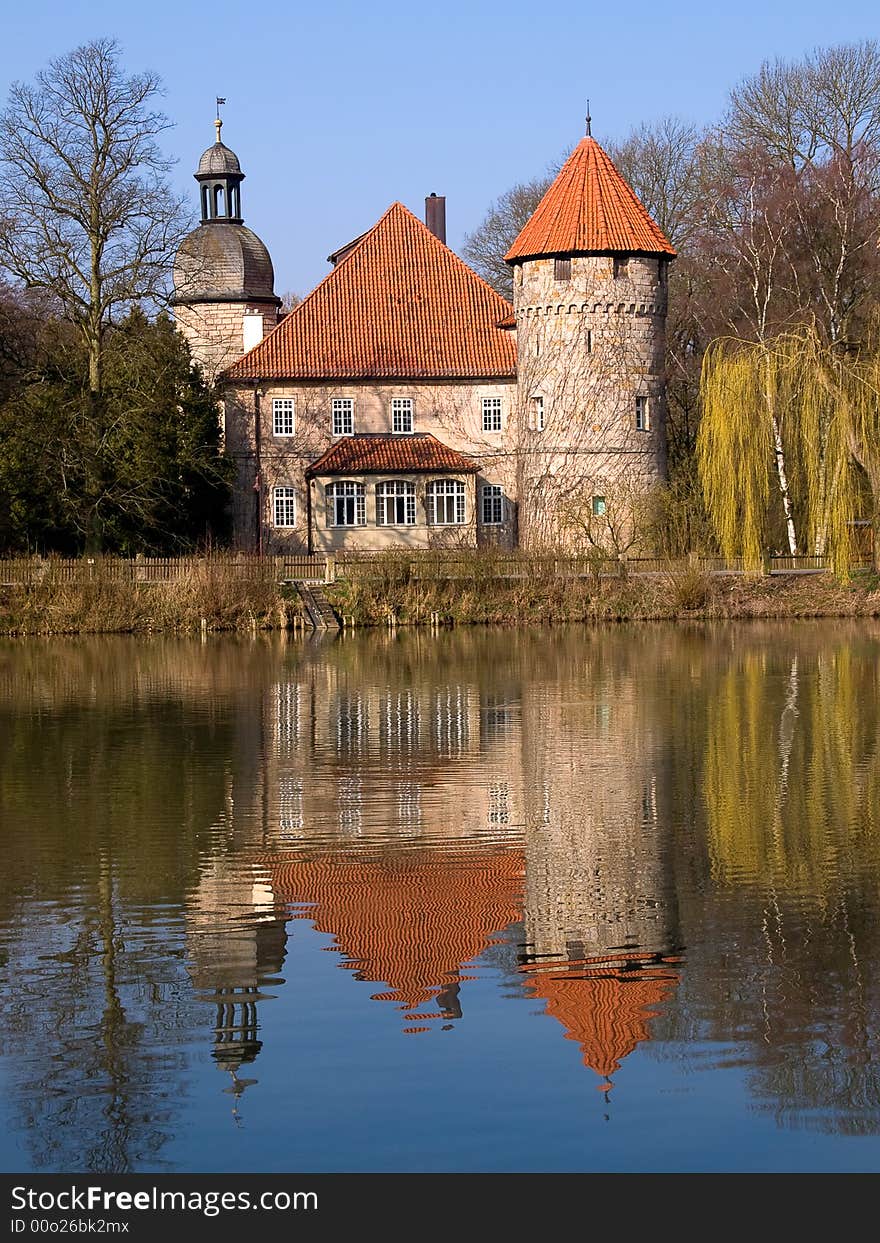 German water castle in bright sunlight 
mirroring in the lake