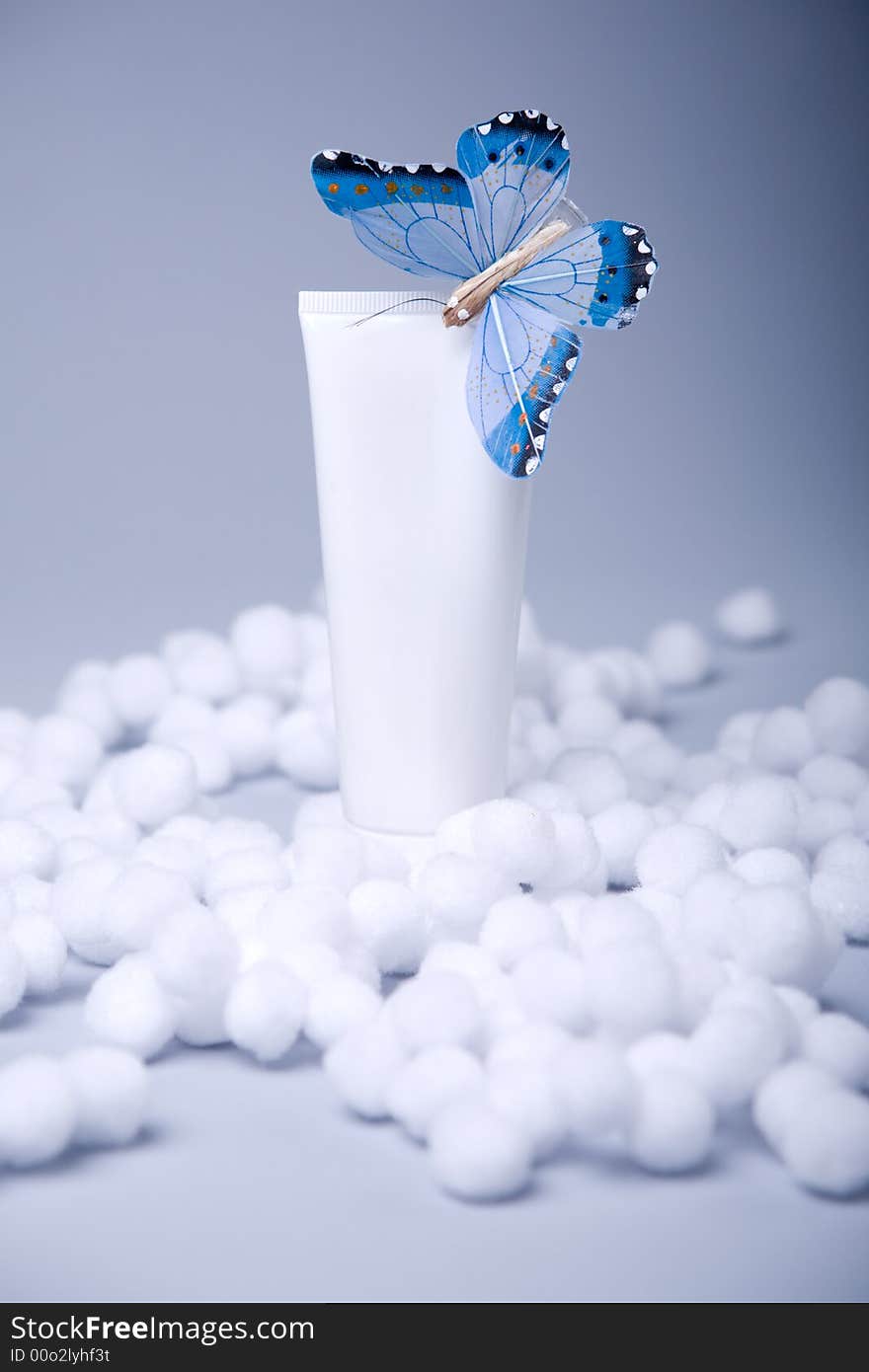 White cosmetic tube with blank area with blue butterfly on blue-gray background in artificial snow. White cosmetic tube with blank area with blue butterfly on blue-gray background in artificial snow