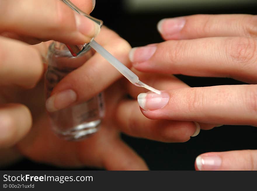 Hands of woman glossing nails of her friend.