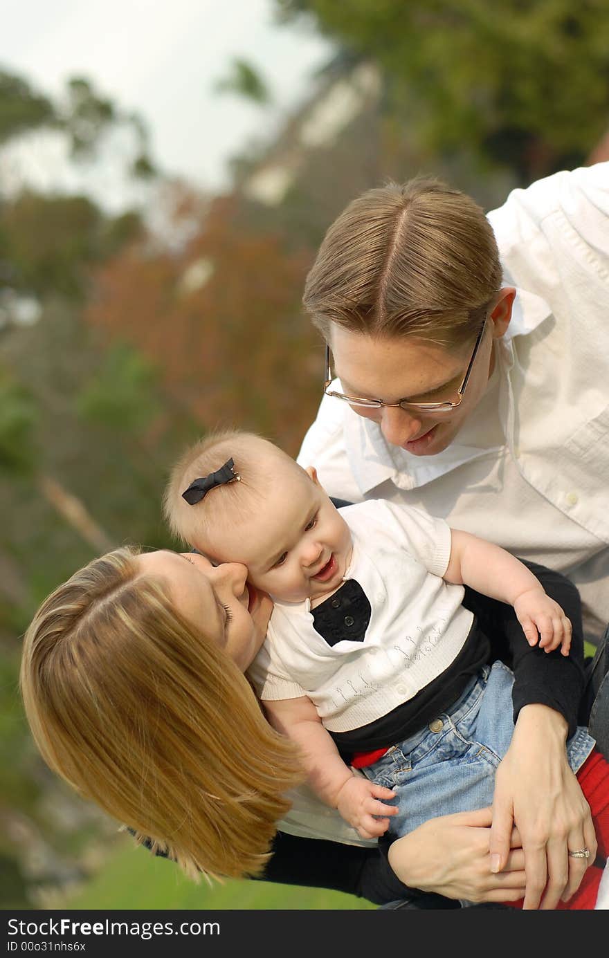 Attractive young parents and their little baby daughter posing for a portrait at the park. Attractive young parents and their little baby daughter posing for a portrait at the park