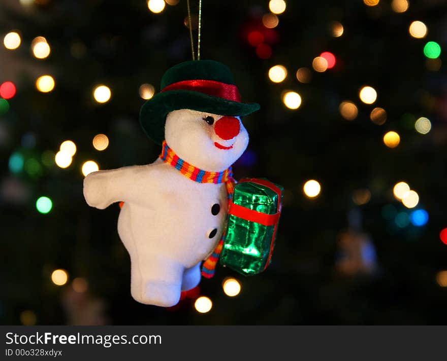 A Frosty the Snowman ornament hangs against a background of shimmering Christmas tree lights. A Frosty the Snowman ornament hangs against a background of shimmering Christmas tree lights