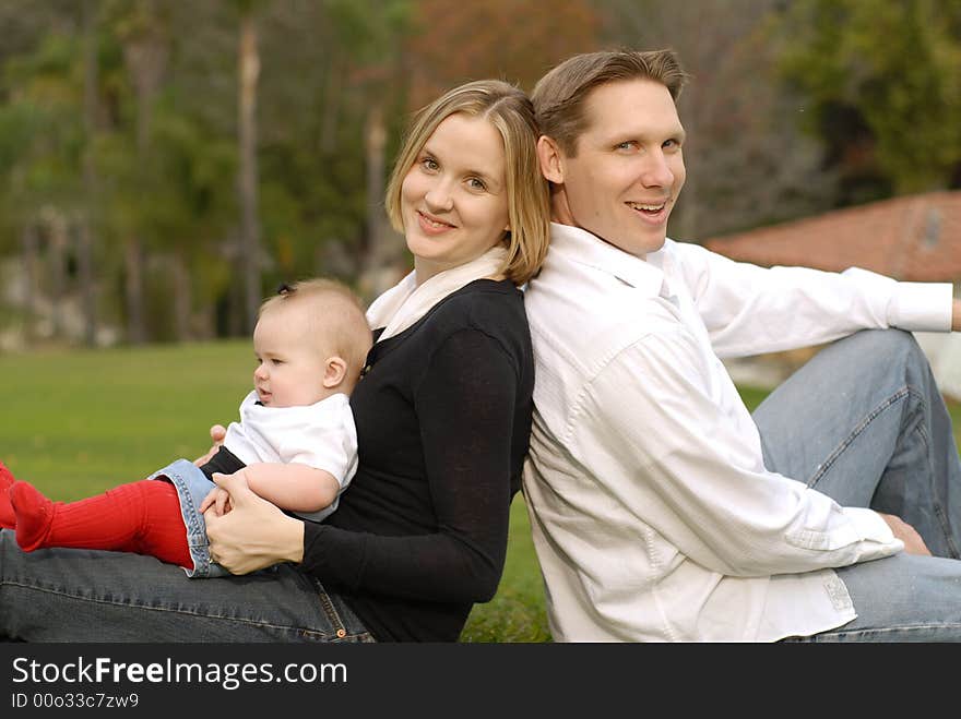 Attractive young family sitting side by side in a park. Attractive young family sitting side by side in a park