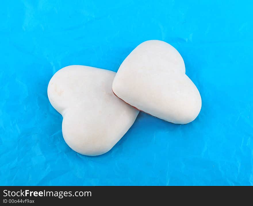 Couple of white honey-cakes hearts over blue paper. Couple of white honey-cakes hearts over blue paper