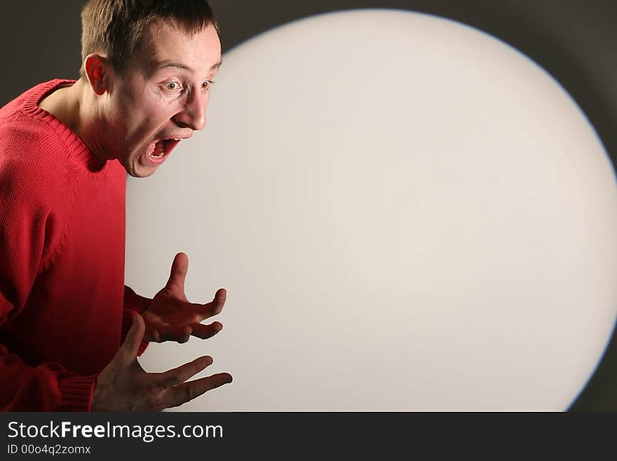 Young man in red pullover screaming and gesticulating - with a white circle in the background. Young man in red pullover screaming and gesticulating - with a white circle in the background.