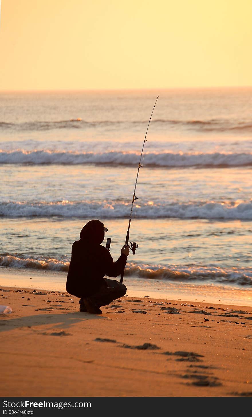 A fisherman, kneeling down surf fishing on a beautiful colorful Summer morning at sunrise. A fisherman, kneeling down surf fishing on a beautiful colorful Summer morning at sunrise.