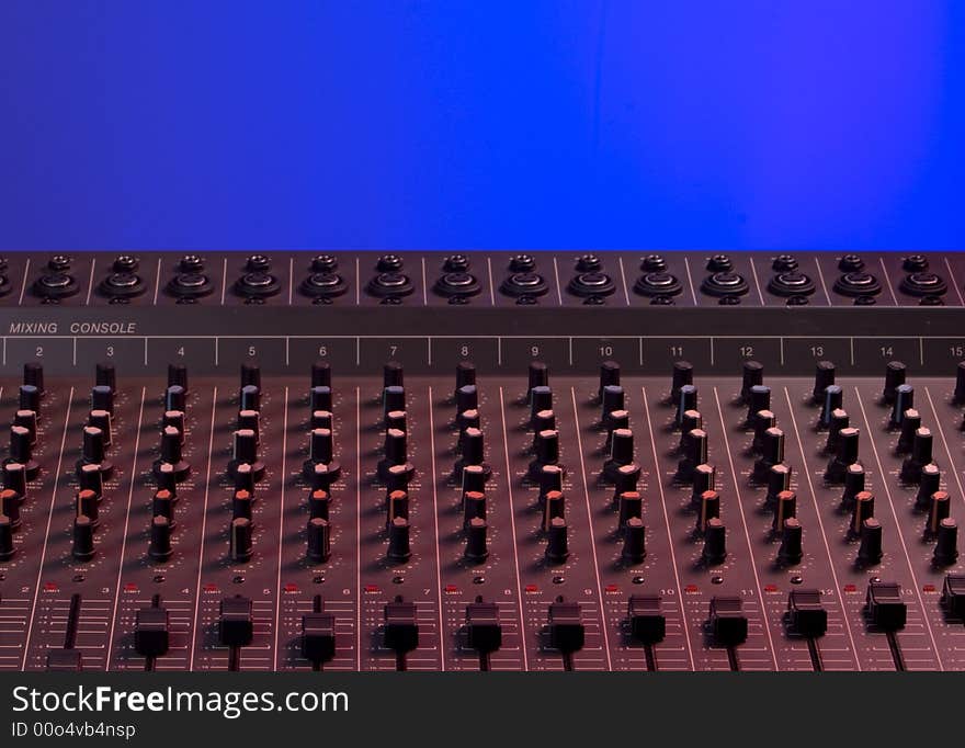 Audio mixing console dramatically lit with red light on blue background. Audio mixing console dramatically lit with red light on blue background