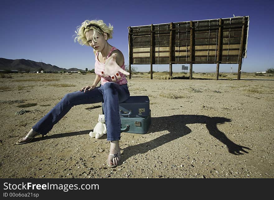 Woman sitting on suitcases in front of an old billboard reaching to the camera. Woman sitting on suitcases in front of an old billboard reaching to the camera