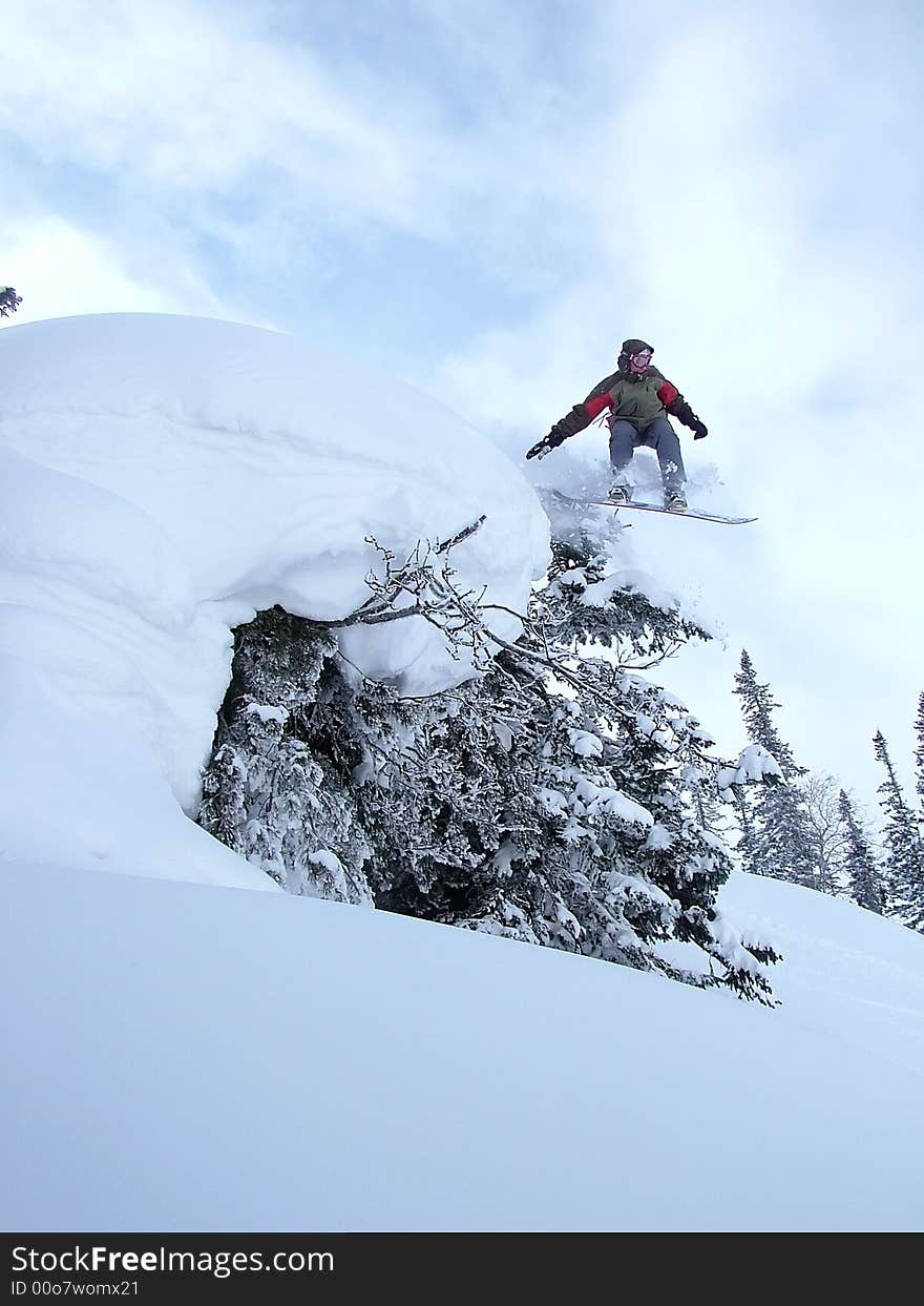 Snowboarder enjoying freeride and jumping high from the snow-capped tree. Snowboarder enjoying freeride and jumping high from the snow-capped tree