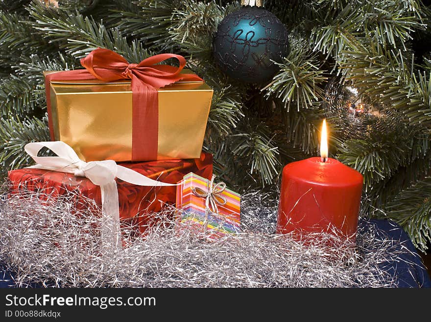 Gifts and burning candle under a Christmas tree. Gifts and burning candle under a Christmas tree