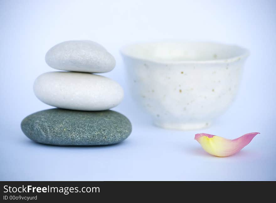 Pyramid of pebbles, cup and rose petal in tranquil still life. Spa series. Pyramid of pebbles, cup and rose petal in tranquil still life. Spa series.