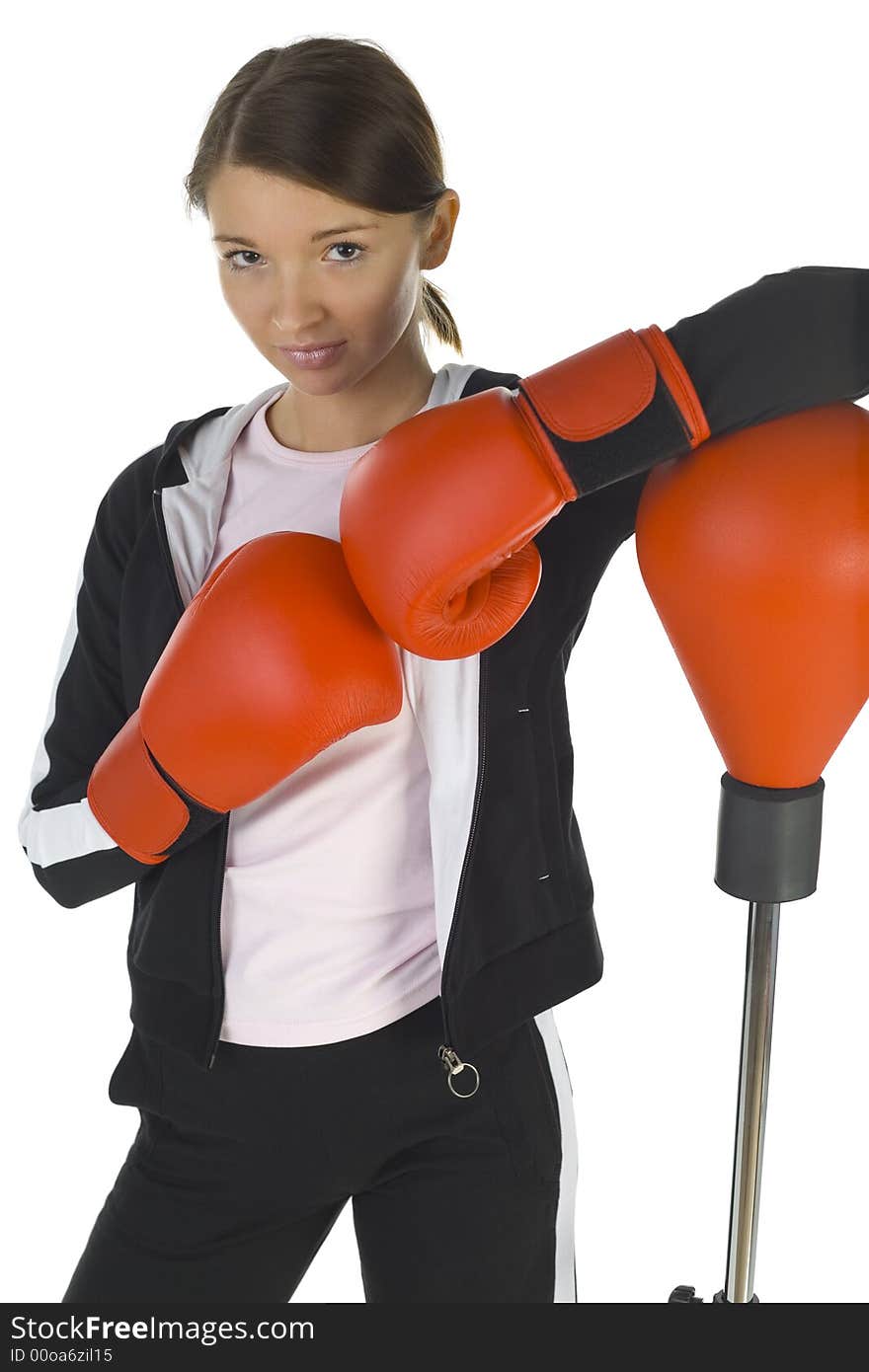 Young beauty with boxing gloves. Standing next to punch bag. Looking at camera. White background, front view. Young beauty with boxing gloves. Standing next to punch bag. Looking at camera. White background, front view