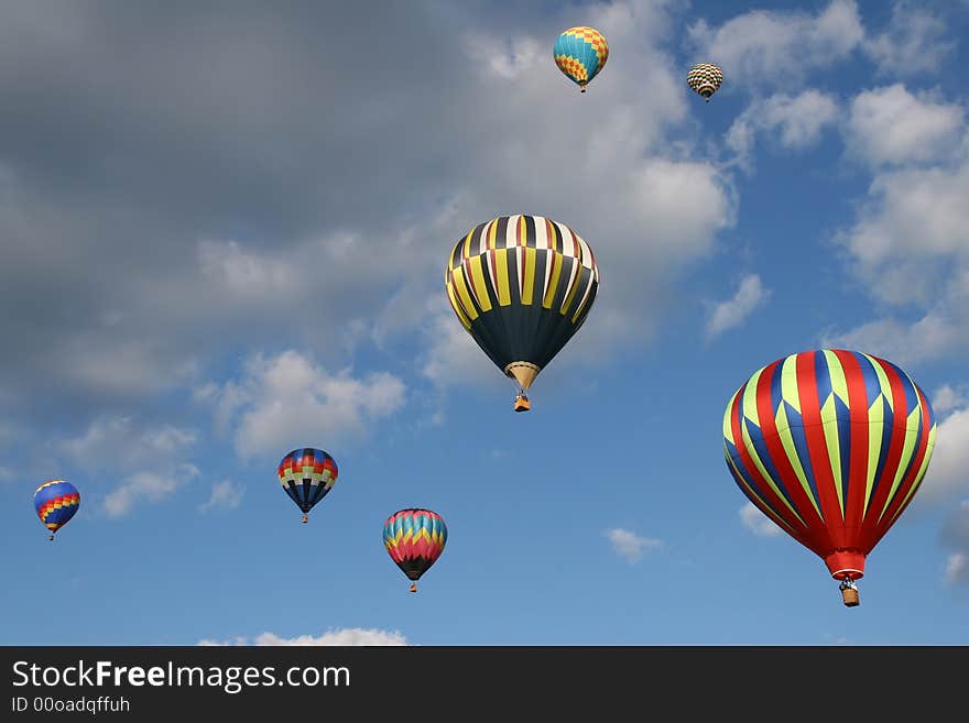 Seven hot air balloons flying in a cloudy blue sky