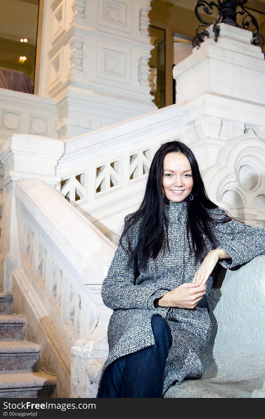 Young beautiful woman in coat sitting in some old style building and smiling. Young beautiful woman in coat sitting in some old style building and smiling