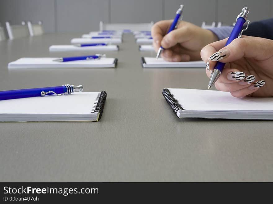 A grey table with grey chairs and notebooks laying on a table and pens