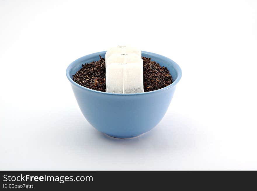 Tea leafs and bags in blue bowl on white background