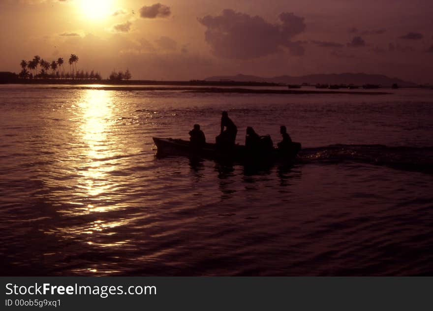 Sunset at Marang in Terengganu, Malaysia as a couple of fishermen in silhouette set out to sea in their boat