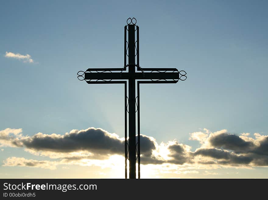 Metal croos against a blue sky with sun behind cloud. Metal croos against a blue sky with sun behind cloud