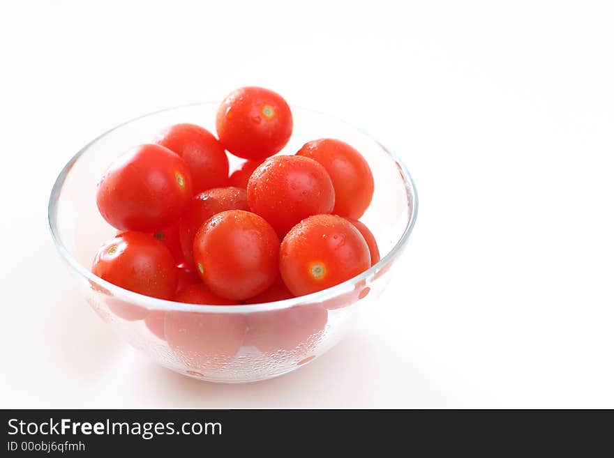 Cherry tomatoes in a transparent glass bowl on a white table-top