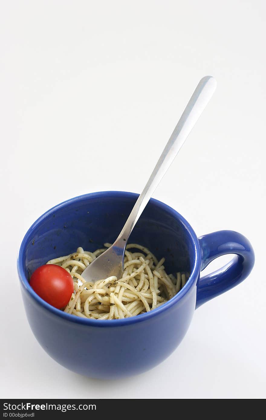 Pasta olio with a cherry tomato in a large blue ceramic cup