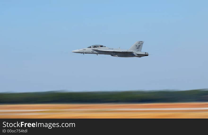 Navy jet plane flying low to the ground showing motion blur to the ground