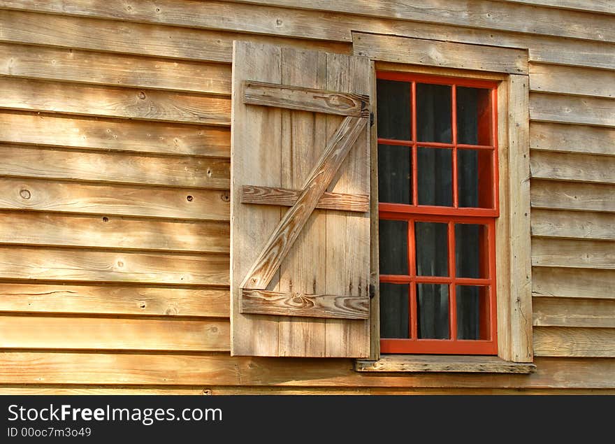 A red window and shutter in a weathered wood building. A red window and shutter in a weathered wood building