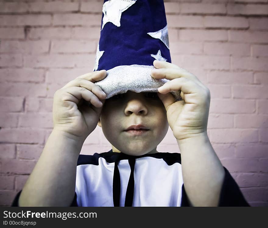 Young boy lifts the brim of a wizard hat and peers out. Young boy lifts the brim of a wizard hat and peers out.