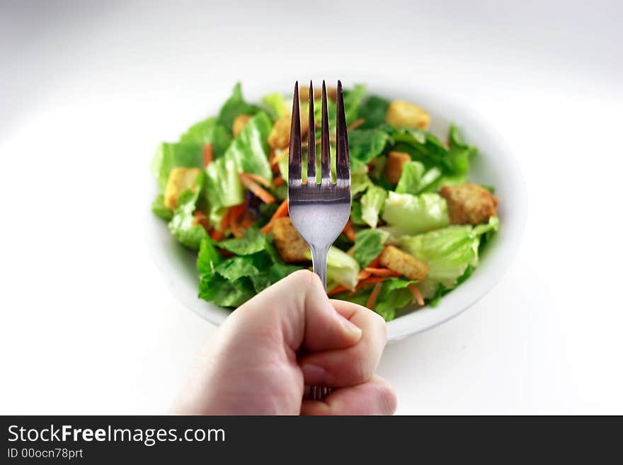 Hand holding fork over generic out of focus salad. Hand holding fork over generic out of focus salad.