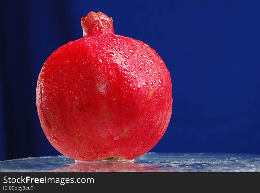 Pomegranate on the glass table over blue background. Pomegranate on the glass table over blue background.