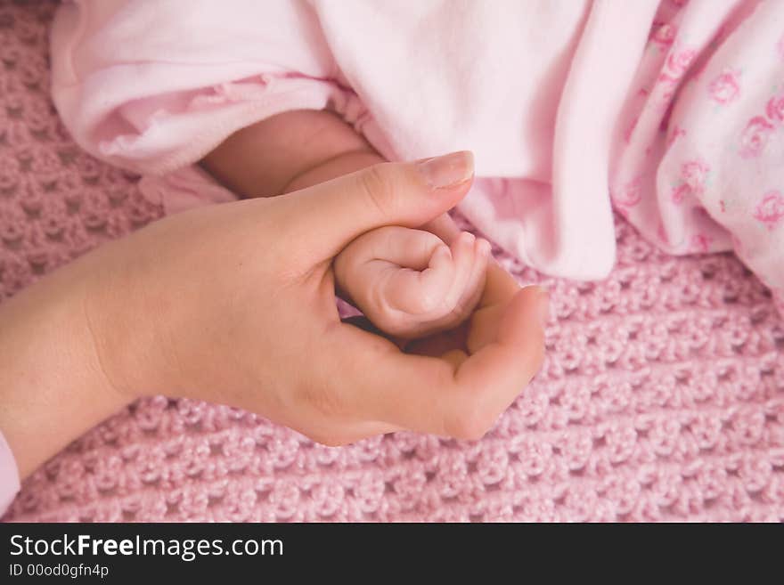 Close up of hands of mother and newborn , baby dressed in pink on a pink knitted background. Close up of hands of mother and newborn , baby dressed in pink on a pink knitted background