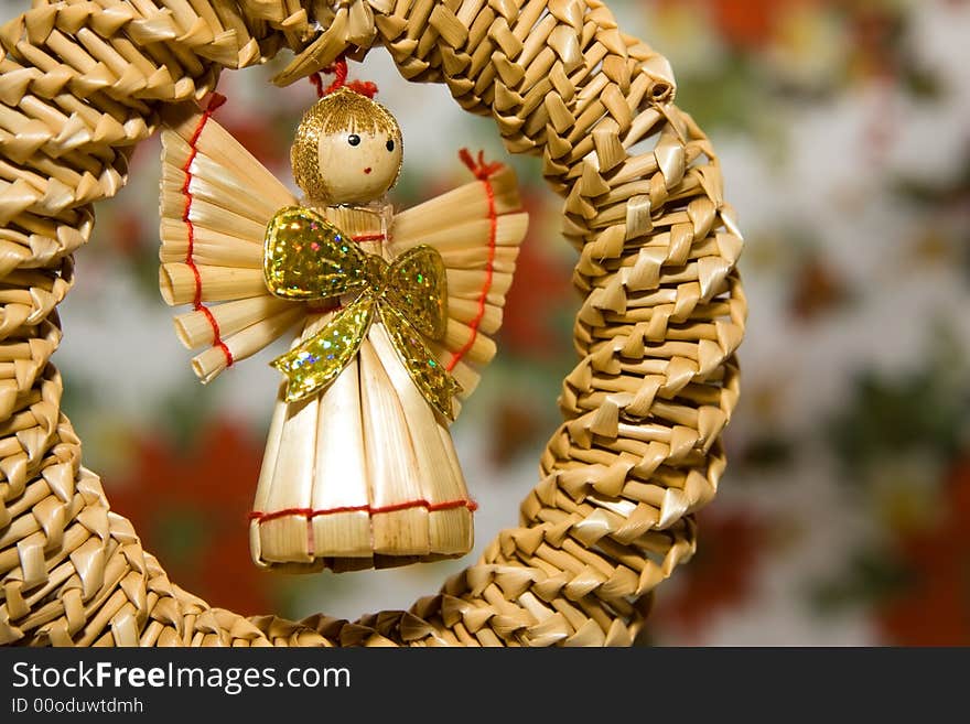 Angel toy made of straw hanging against colorful background.