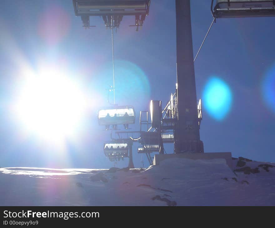 Sun over ski-lift in snowy mountain scene. Sun over ski-lift in snowy mountain scene