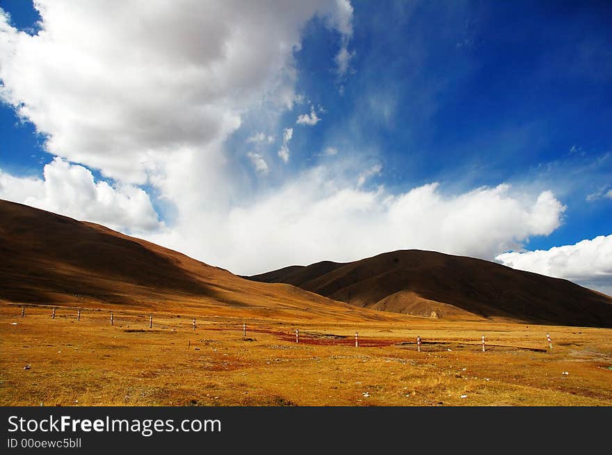 The empty grass land with blue sky and grand cloud. The cloud makes big shadow on the empty grass land. The view of west China usually shocks travelers. The empty grass land with blue sky and grand cloud. The cloud makes big shadow on the empty grass land. The view of west China usually shocks travelers.