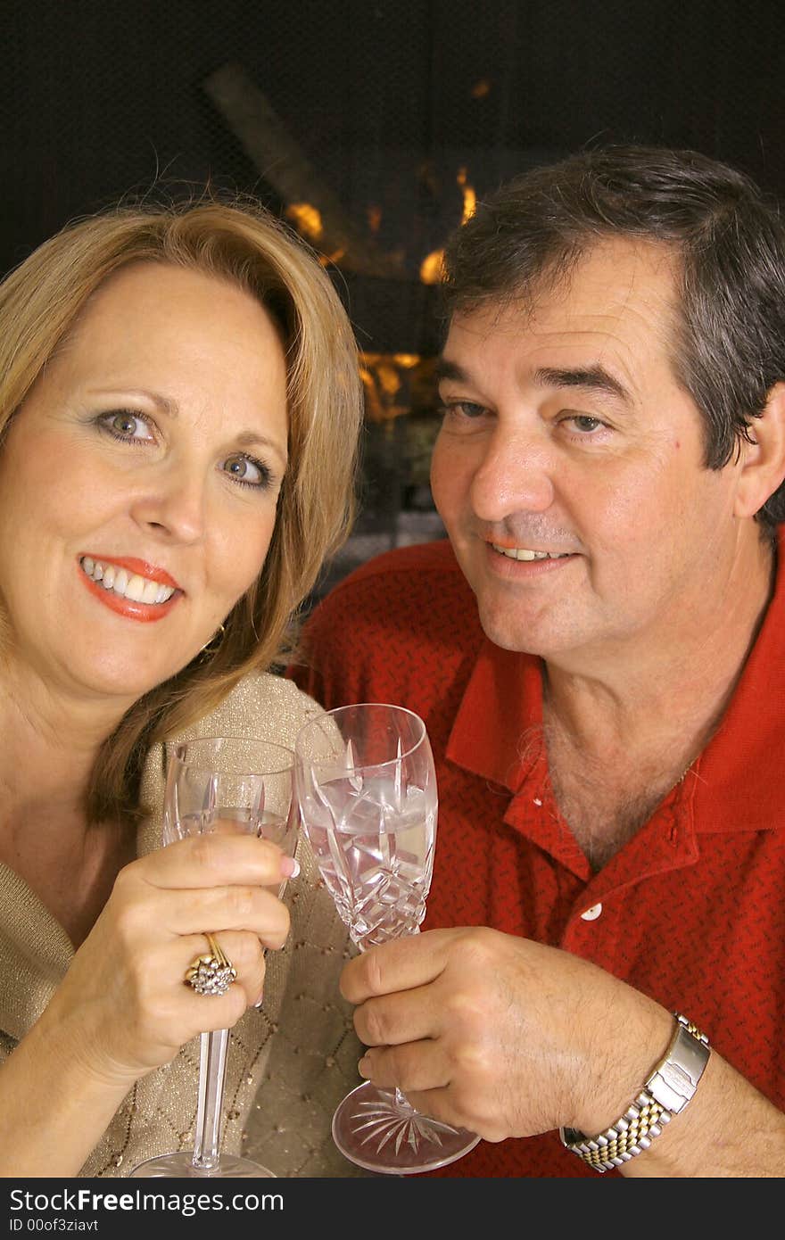 Happy couple toasting in front of a fireplace