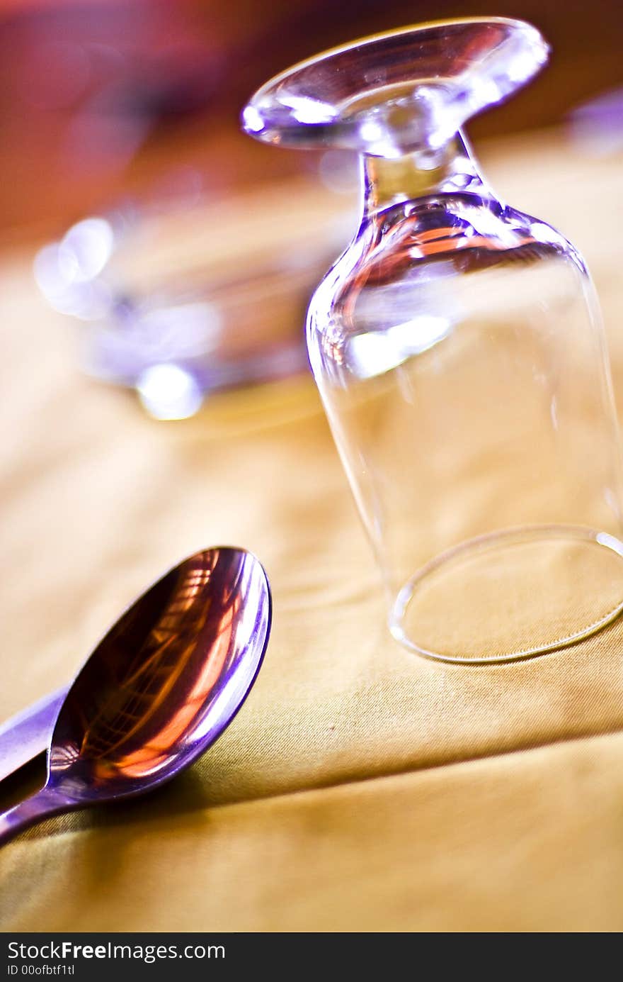 A closeup view of an upside-down drinking glass and a spoon nearby on a table.  . A closeup view of an upside-down drinking glass and a spoon nearby on a table.