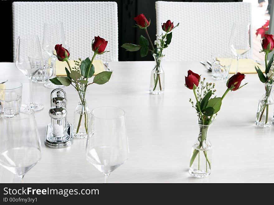 Elegant table setting with vases of red roses and white linen.