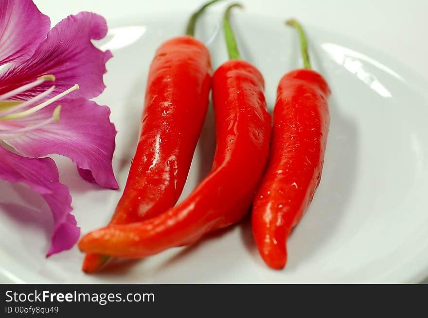 Three red chilies on the plate and a flower.