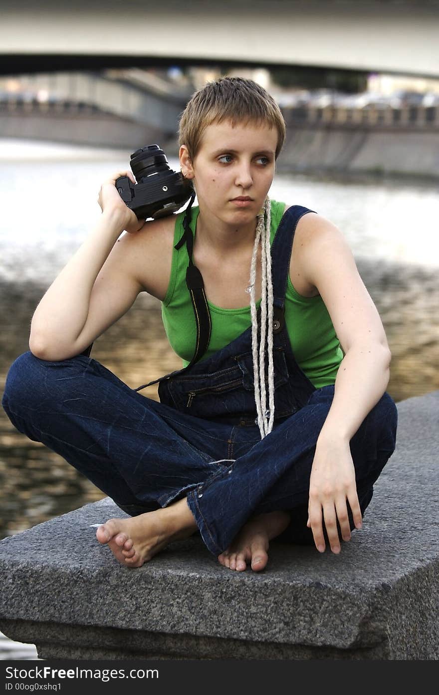 Sad young girl photographer sitting near the city river. Sad young girl photographer sitting near the city river