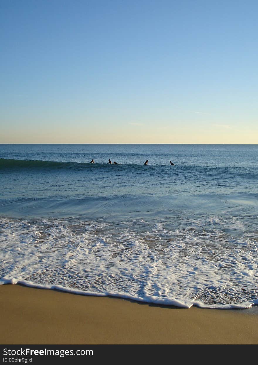 5 surfers waiting on their surfboards for the perfect wave