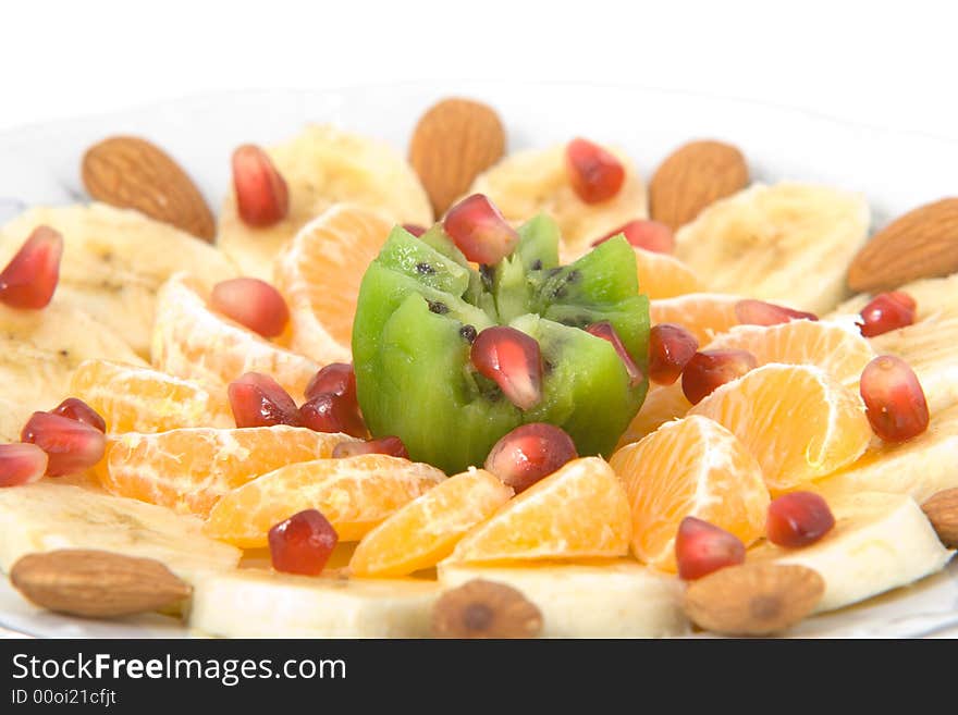 Delicious fruit salad made of kiwi, tangerines, bananas, almonds and pomegranate on white round plate isolated on white. Delicious fruit salad made of kiwi, tangerines, bananas, almonds and pomegranate on white round plate isolated on white