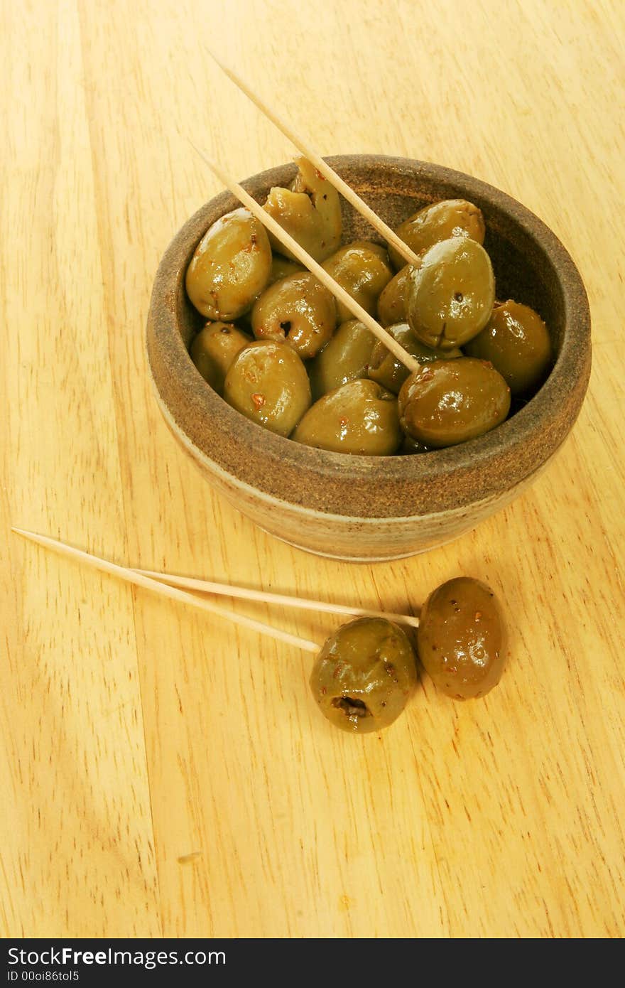 A bowl of olives with cocktail sticks on a wooden board