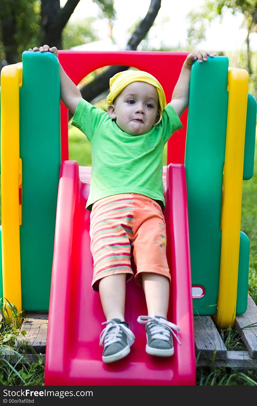 A cute caucasian boy playing on a colorful slide outdoors. A cute caucasian boy playing on a colorful slide outdoors.