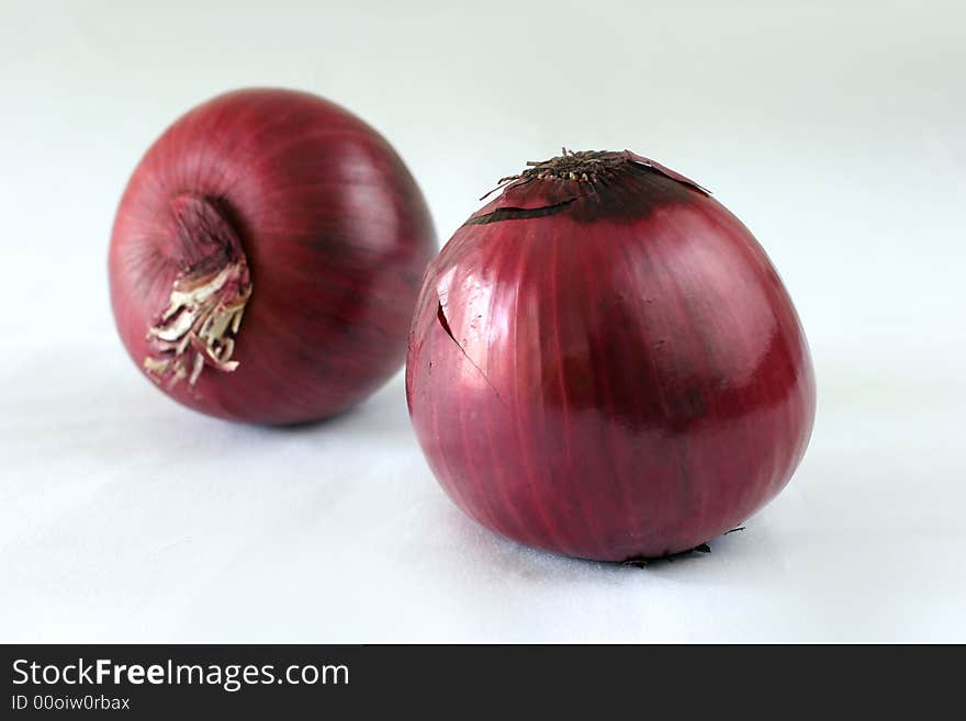 Two large, whole, raw purple Dutch beauty onions on a white table top