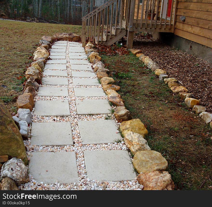 A stepping stone and pebble walkway surrounded by river rocks leading up to red front door and front porch.